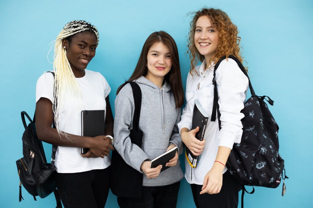 happy multiethnic female students standing together on blue background