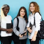 happy multiethnic female students standing together on blue background
